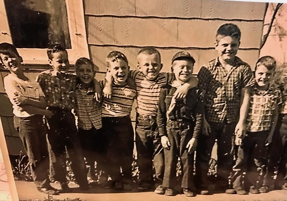 A group of seven young boys standing together outdoors, smiling.