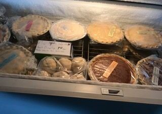 Various pies and baked goods wrapped in plastic on a refrigerated shelf.