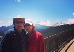 Couple posing on a mountain boardwalk under a clear sky.