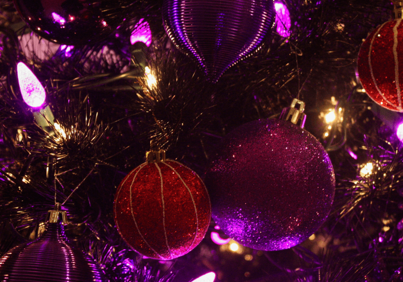 Purple and red ornaments decorate a glowing Christmas tree.