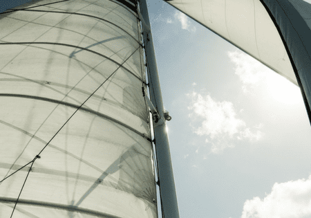 Close-up view of a sailboat mast and sail against a partly cloudy sky.