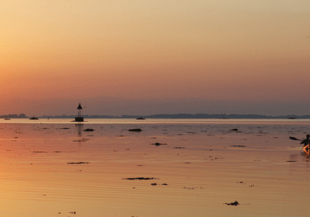 Kayaker paddling across calm sunset bay