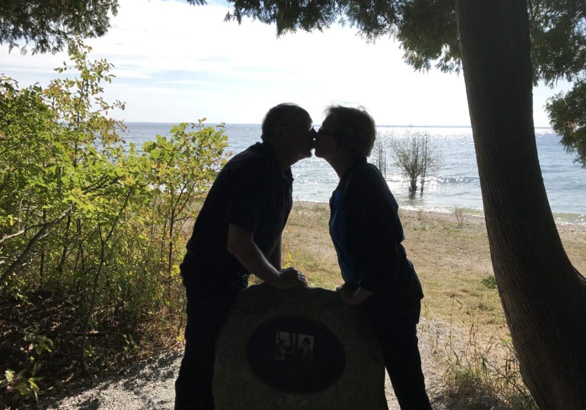 Silhouetted couple kissing by lakeshore under trees
