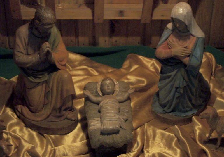 Nativity scene with baby Jesus and figures of Mary and Joseph on golden cloth.