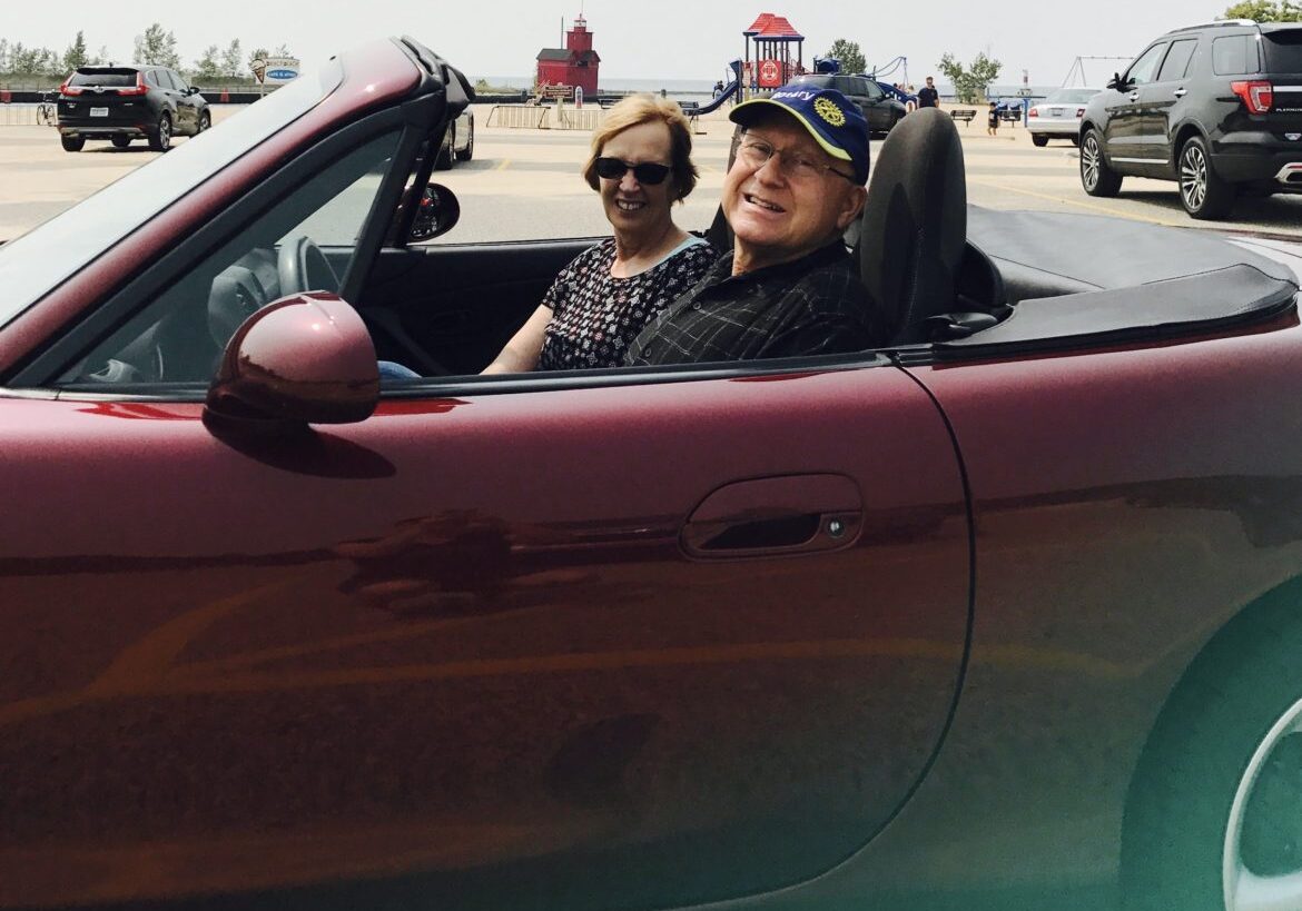 Two women smiling in a red convertible car on a sunny day.