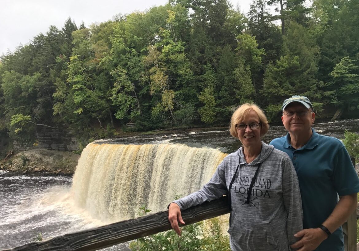 Couple posing in front of a scenic waterfall surrounded by lush greenery.