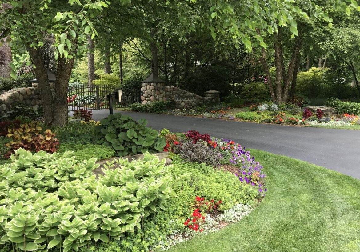 Curved driveway through lush garden with stone gate